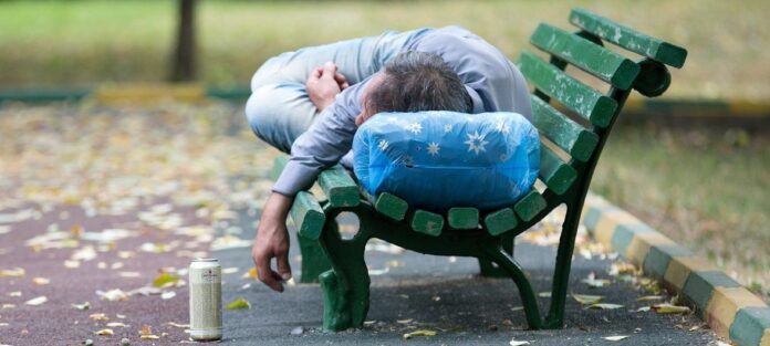 Um homem embriagado está dormindo em um banco de um parque
